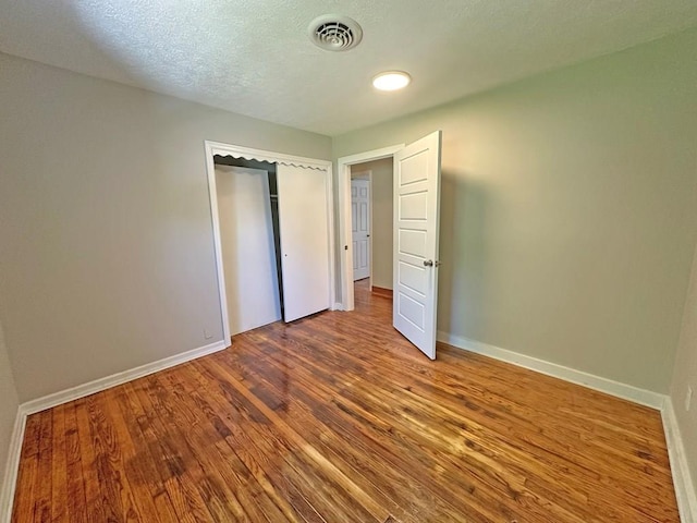 unfurnished bedroom with a textured ceiling, wood finished floors, visible vents, and baseboards