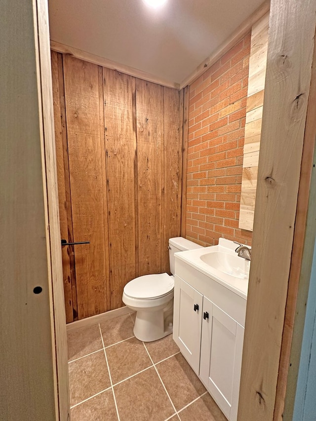 half bath with tile patterned floors, toilet, wood walls, and vanity