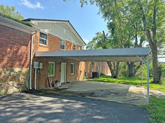 view of front of property with a carport, central AC unit, brick siding, and driveway