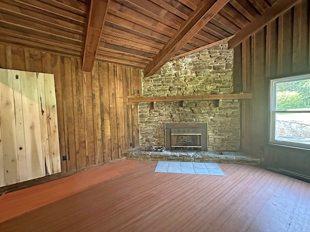 unfurnished living room with beamed ceiling, wood walls, a stone fireplace, wooden ceiling, and wood finished floors