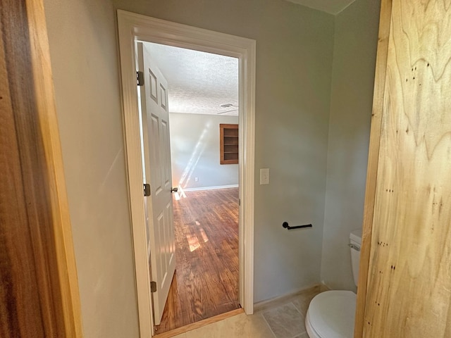 bathroom with toilet, a textured ceiling, baseboards, and wood finished floors