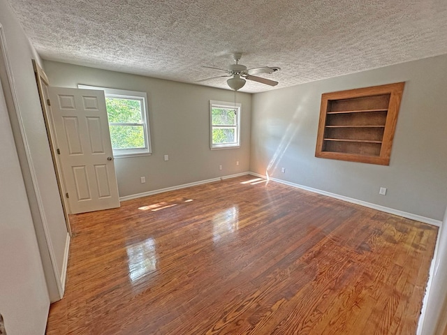 empty room featuring built in shelves, ceiling fan, baseboards, wood finished floors, and a textured ceiling