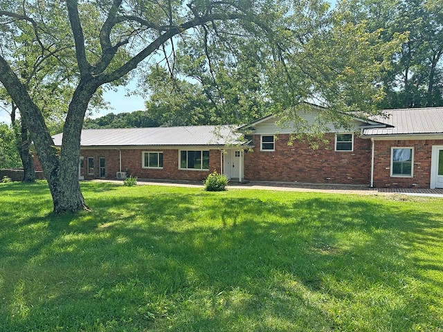 view of front of house featuring metal roof, brick siding, and a front yard