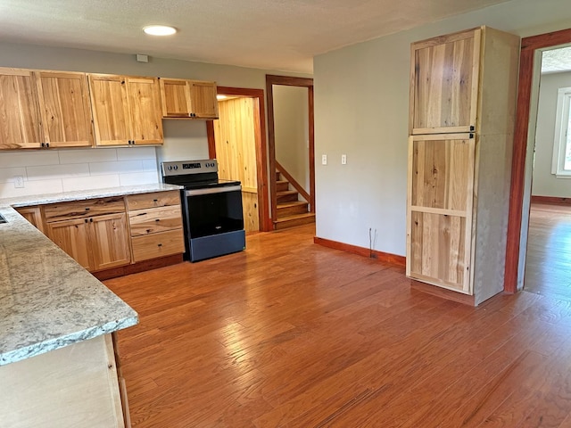 kitchen featuring light stone countertops, baseboards, electric range, light wood-style floors, and backsplash