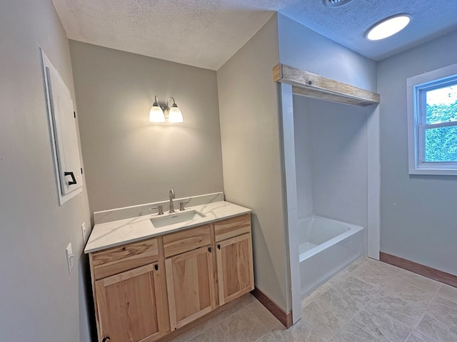 bathroom with a bathtub, baseboards, a textured ceiling, and vanity