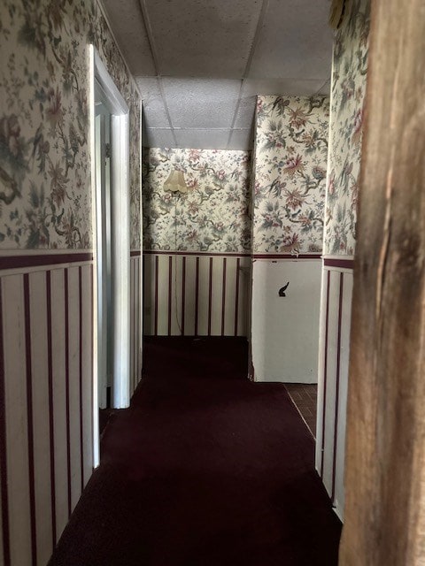 hall featuring a wainscoted wall and wallpapered walls