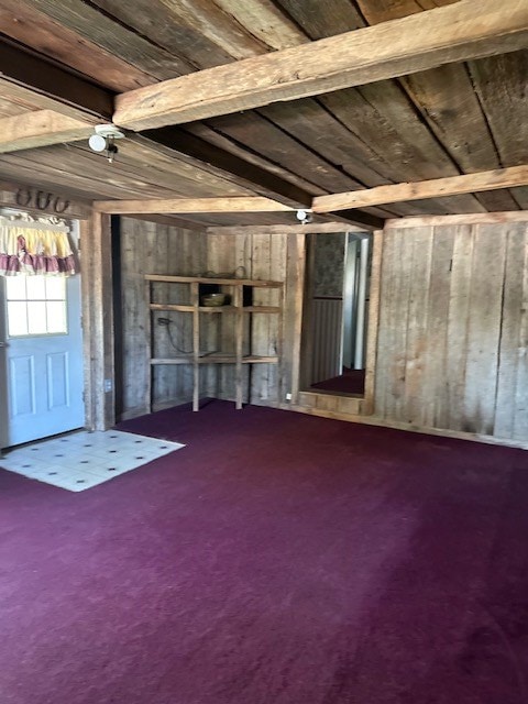 unfurnished living room featuring wood walls, wood ceiling, beam ceiling, and carpet flooring