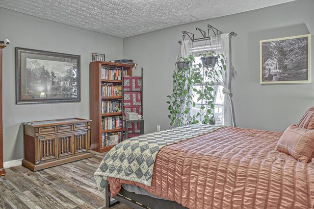 bedroom with a textured ceiling, baseboards, and wood finished floors