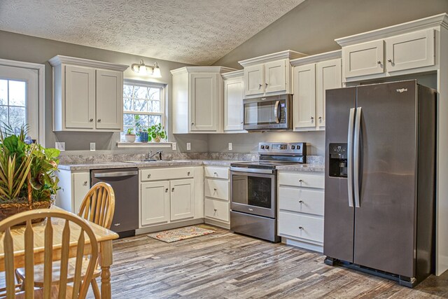 kitchen featuring lofted ceiling, appliances with stainless steel finishes, light wood-style floors, white cabinetry, and a sink