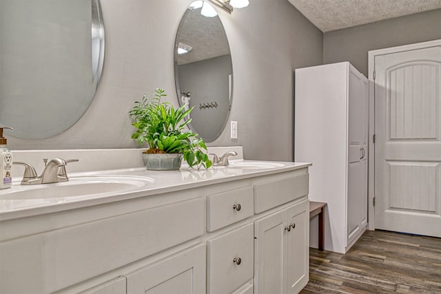 bathroom featuring double vanity, a textured ceiling, a sink, and wood finished floors