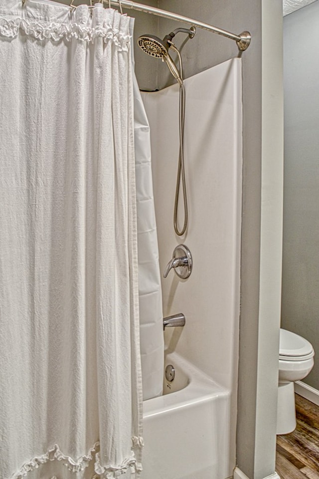 bathroom featuring baseboards, shower / bathtub combination with curtain, toilet, and wood finished floors