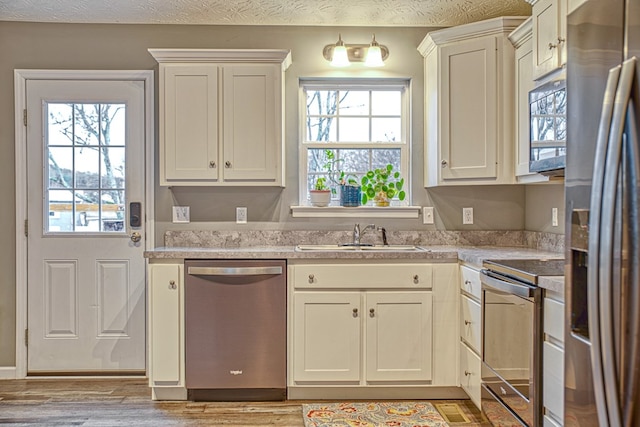 kitchen with white cabinets, appliances with stainless steel finishes, light countertops, light wood-style floors, and a sink