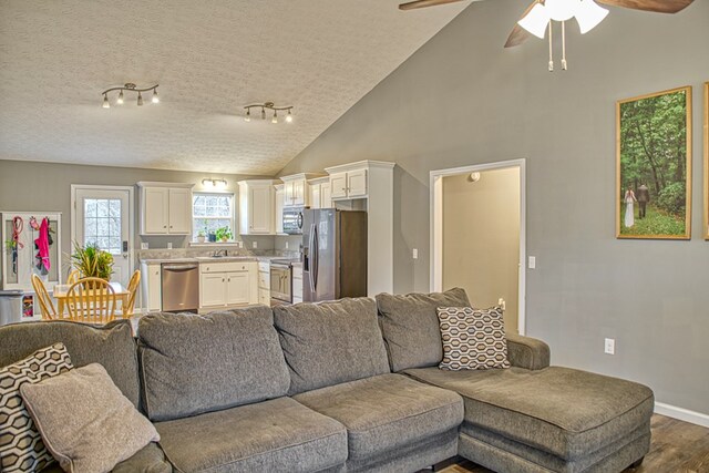 living room with dark wood-style flooring, a ceiling fan, a textured ceiling, high vaulted ceiling, and baseboards