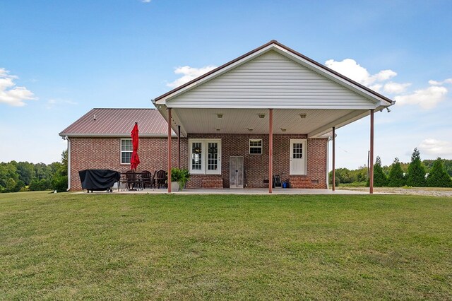 back of house featuring entry steps, metal roof, brick siding, a lawn, and a patio area