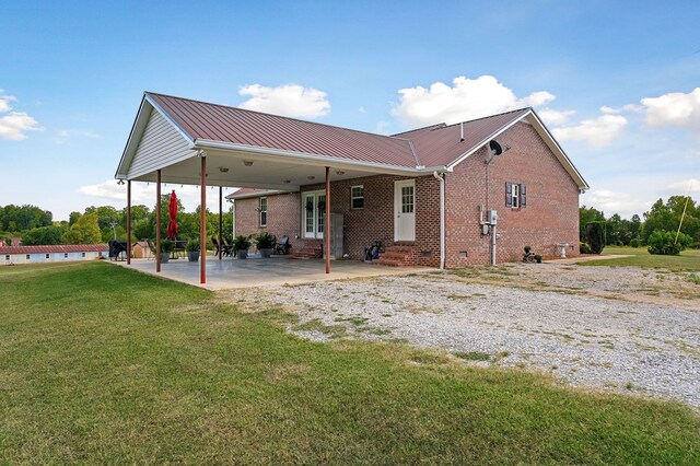 back of house featuring entry steps, a patio, an attached carport, brick siding, and a lawn