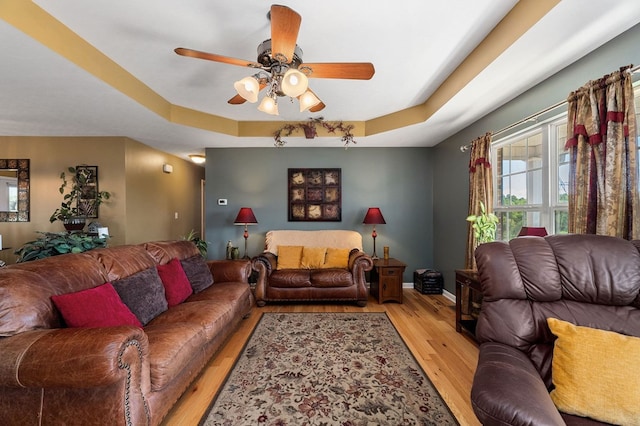 living room with light wood-style floors, a raised ceiling, ceiling fan, and baseboards