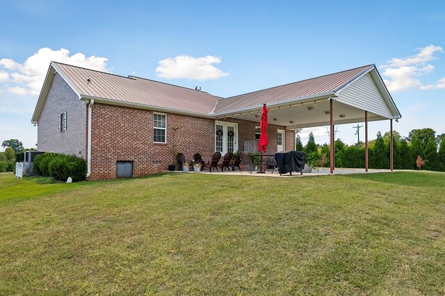 rear view of property with metal roof, brick siding, a patio, and a lawn