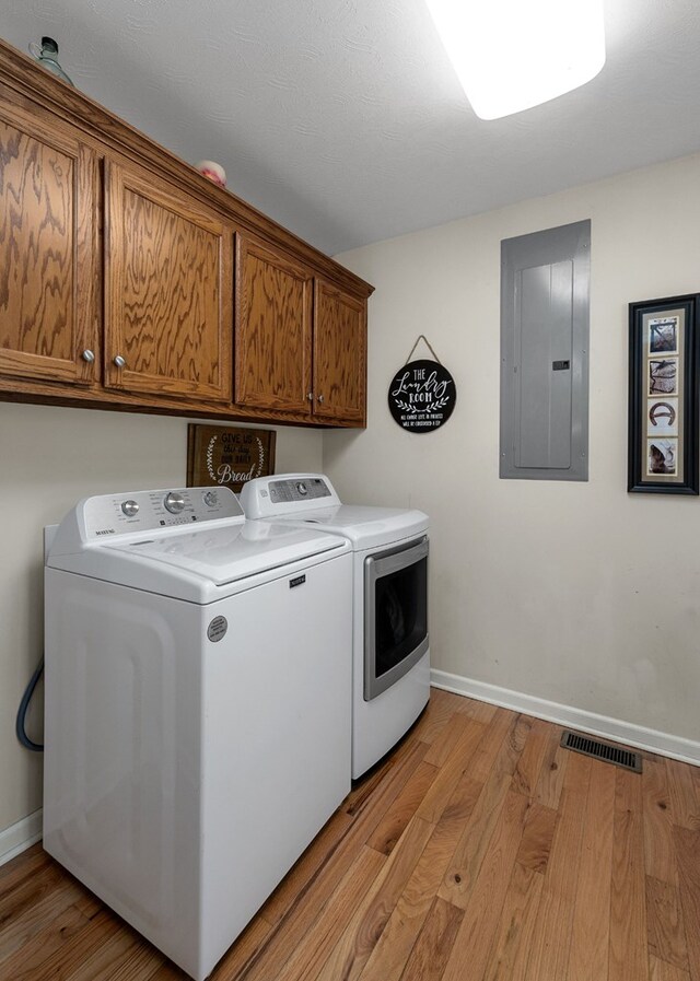 washroom featuring cabinet space, light wood-style flooring, washer and dryer, electric panel, and baseboards