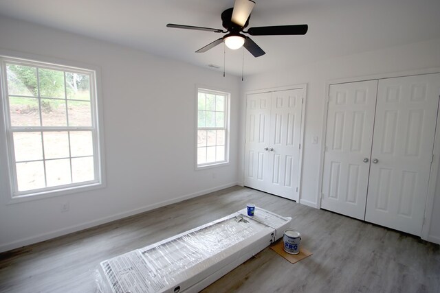 unfurnished bedroom featuring multiple closets, visible vents, light wood-style floors, a ceiling fan, and baseboards