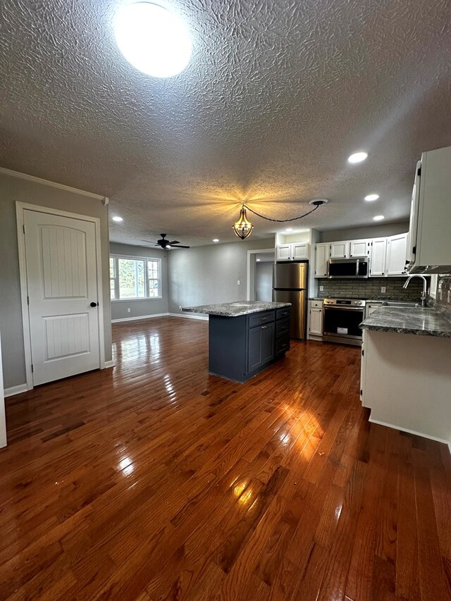 kitchen with stainless steel appliances, white cabinets, open floor plan, a center island, and dark wood finished floors