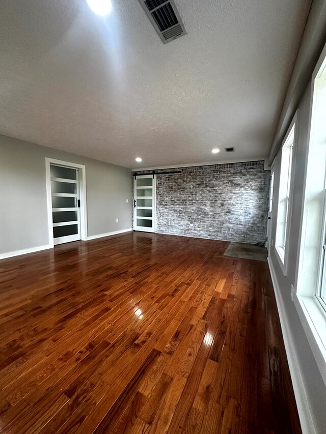 unfurnished living room featuring baseboards, visible vents, built in features, dark wood-type flooring, and a textured ceiling