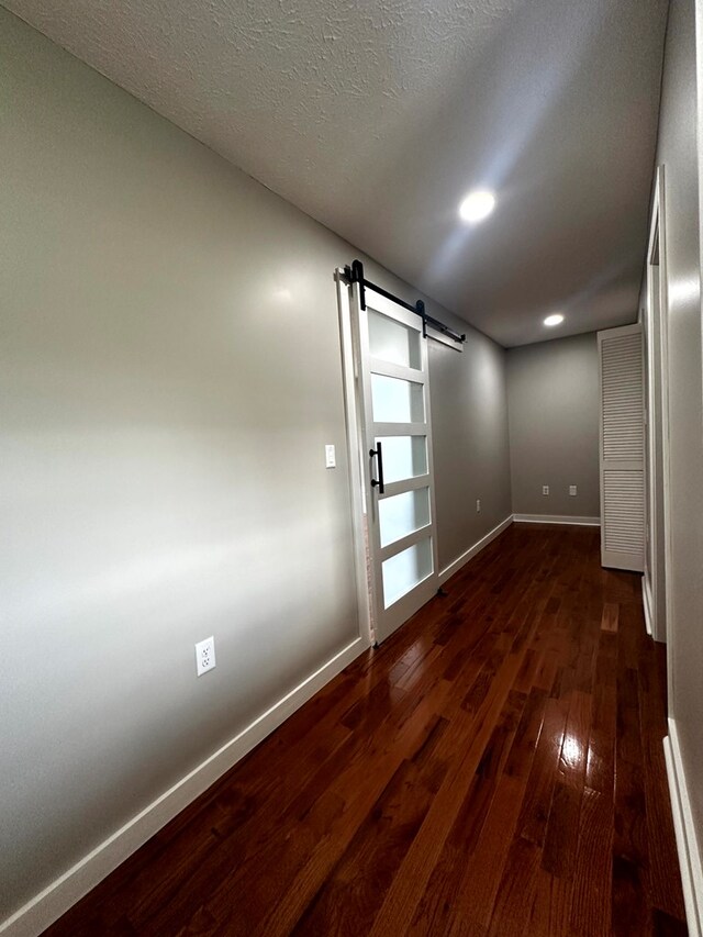 spare room with a textured ceiling, a barn door, recessed lighting, dark wood-style flooring, and baseboards