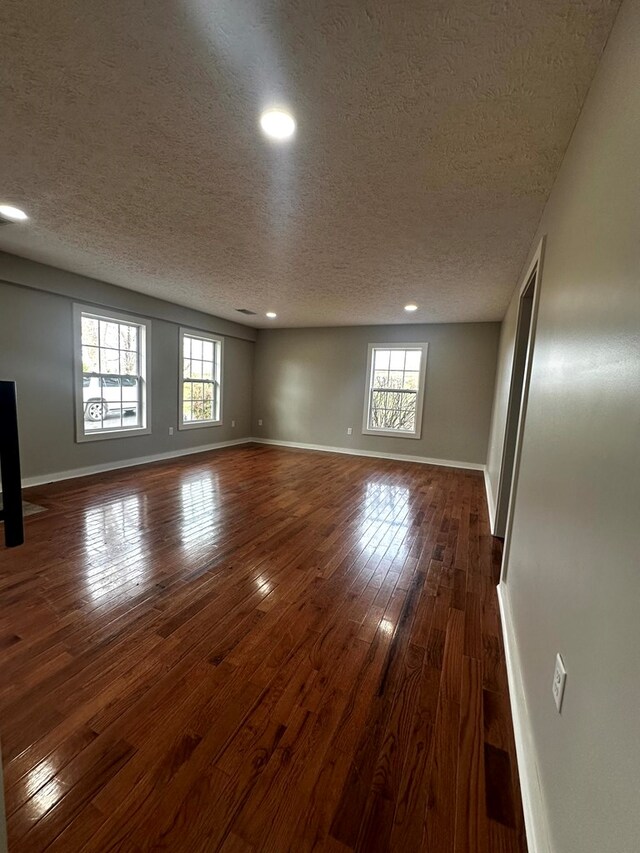 empty room with dark wood-style floors, a textured ceiling, and baseboards