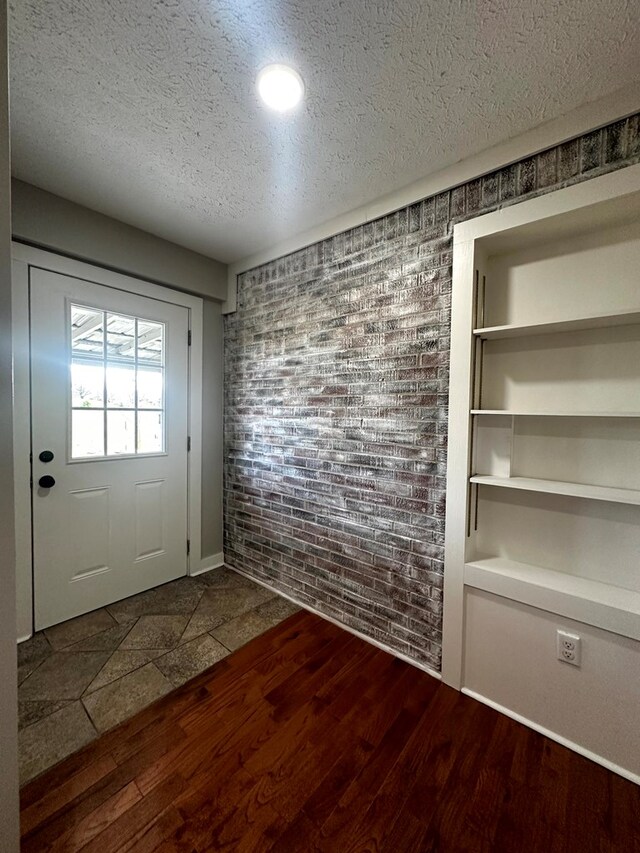 doorway to outside with brick wall, built in features, a textured ceiling, and wood finished floors