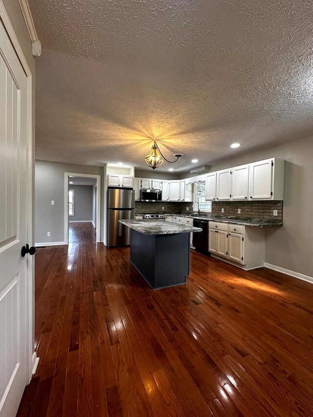 kitchen with appliances with stainless steel finishes, white cabinets, a kitchen island, and backsplash