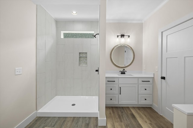 full bathroom with ornamental molding, vanity, wood finished floors, tiled shower, and baseboards