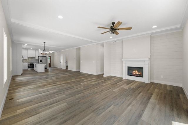 unfurnished living room featuring ceiling fan with notable chandelier, dark wood-type flooring, a glass covered fireplace, and ornamental molding