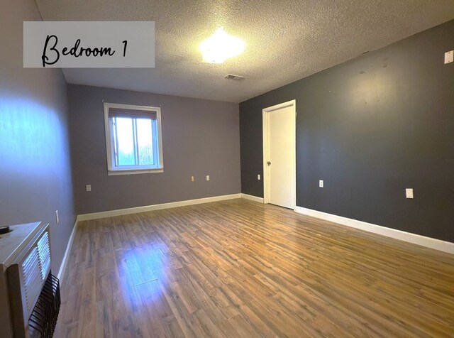 unfurnished room featuring a textured ceiling, wood finished floors, visible vents, and baseboards