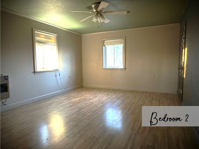 empty room with heating unit, a textured ceiling, a ceiling fan, and wood finished floors