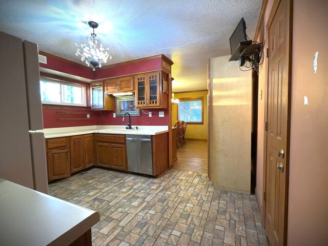 kitchen with brown cabinetry, glass insert cabinets, hanging light fixtures, light countertops, and stainless steel dishwasher