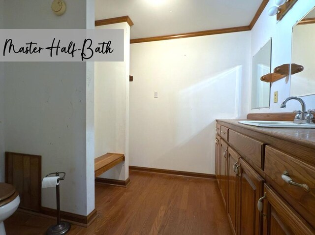 bathroom with toilet, wood finished floors, vanity, baseboards, and ornamental molding