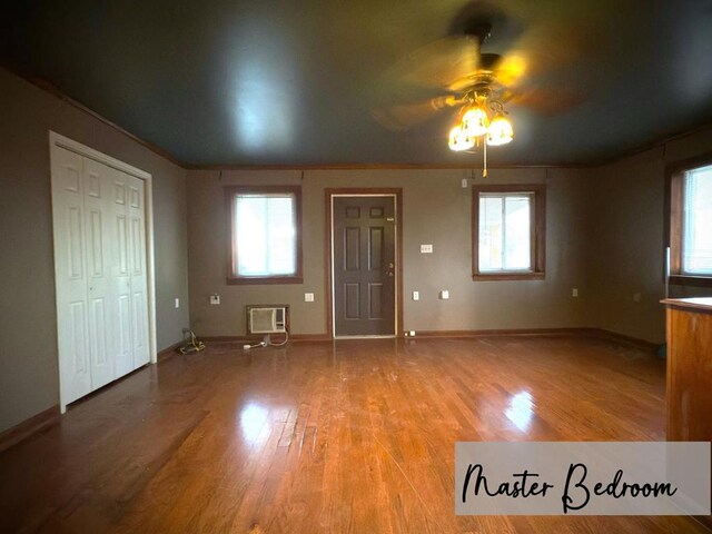 interior space with a wall mounted AC, baseboards, a wealth of natural light, and wood finished floors