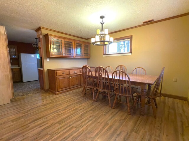 dining area with crown molding, visible vents, an inviting chandelier, a textured ceiling, and wood finished floors