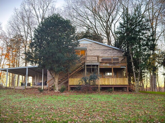 back of house with an attached carport, brick siding, stairs, a yard, and a wooden deck