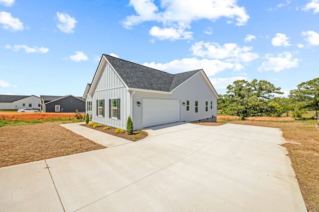 view of property exterior featuring a garage, driveway, a shingled roof, and board and batten siding