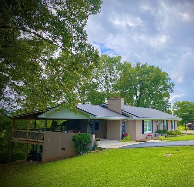 ranch-style home with driveway, metal roof, a chimney, and a front lawn