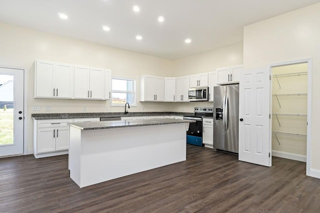 kitchen featuring stainless steel appliances, dark wood-style flooring, a kitchen island, white cabinets, and dark stone countertops