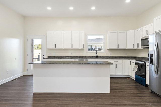 kitchen featuring dark stone counters, white cabinets, appliances with stainless steel finishes, dark wood-type flooring, and a center island