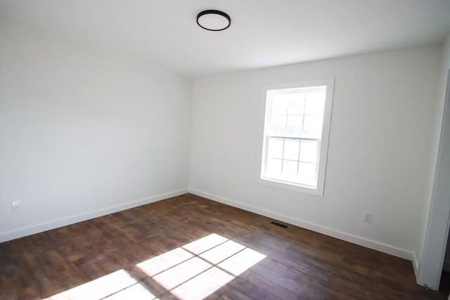 empty room with dark wood finished floors, visible vents, and baseboards