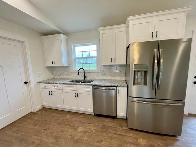 kitchen featuring stainless steel appliances, wood finished floors, a sink, white cabinets, and light stone countertops