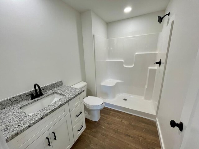 bathroom with a stall shower, vanity, toilet, and wood finished floors