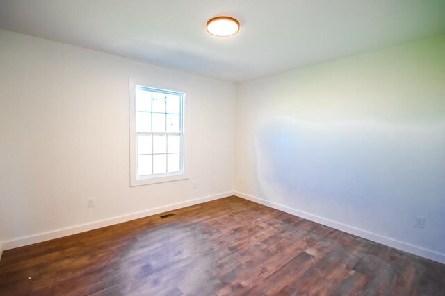 spare room featuring baseboards, visible vents, and dark wood-style flooring