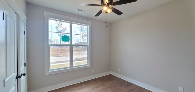 unfurnished room featuring dark wood-type flooring, a wealth of natural light, visible vents, and baseboards