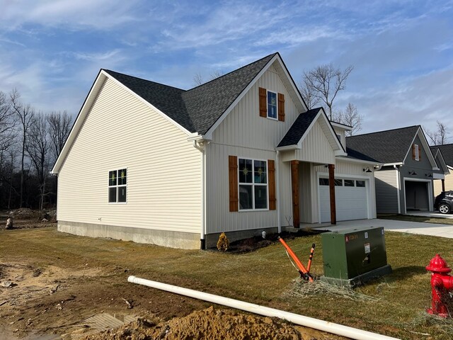 view of side of property with a garage, driveway, roof with shingles, and a lawn