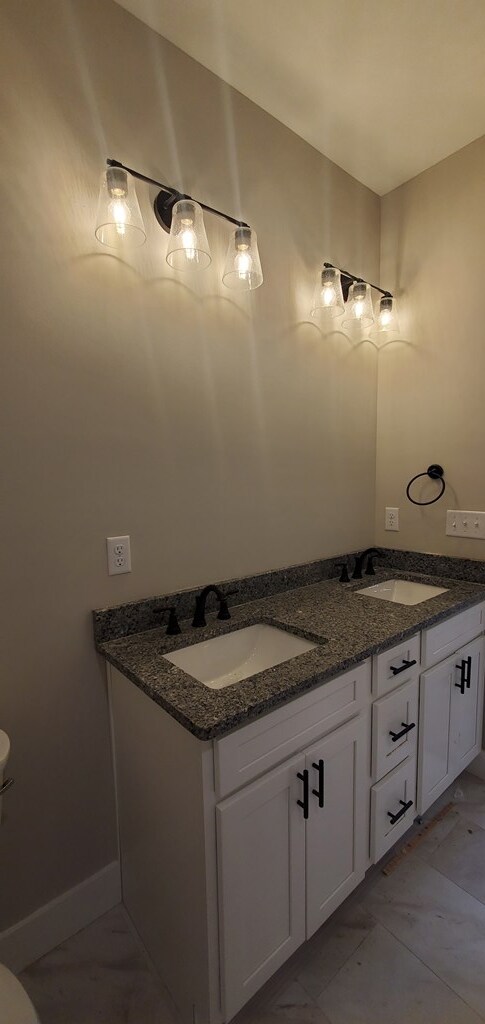 bathroom featuring double vanity, a sink, toilet, and baseboards