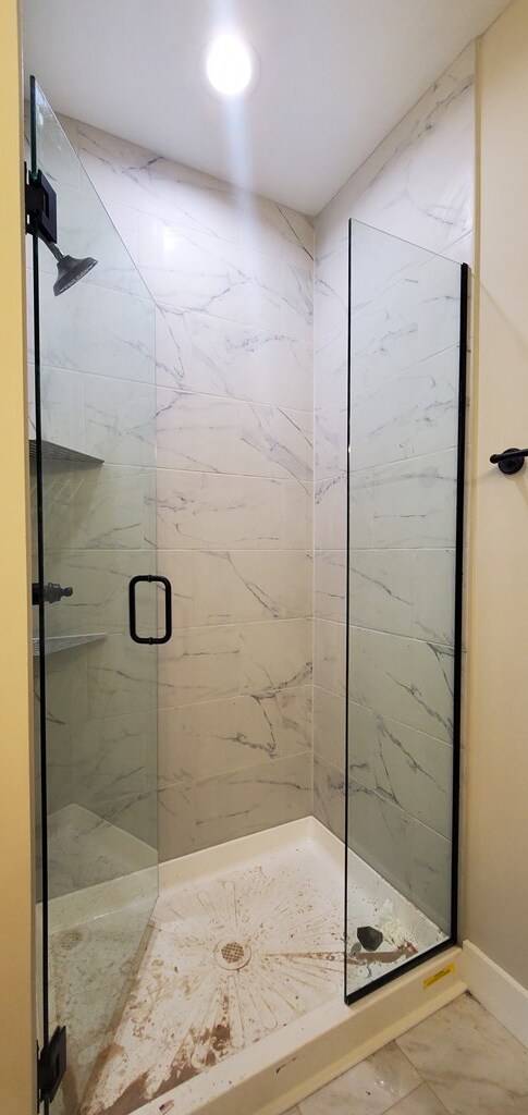 full bathroom with marble finish floor, a shower stall, and baseboards